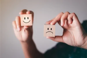 2 hands holding wooden blocks with a sad face and a happy face